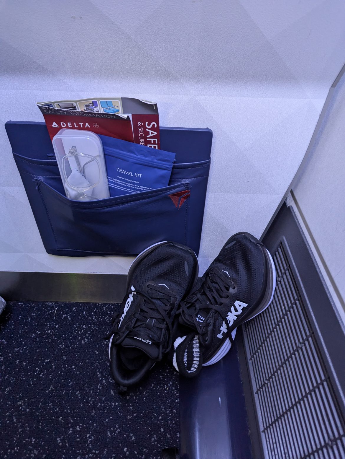 Zapatillas HOKA para fascitis plantar en un avión, junto a un kit de viaje y artículos de cabina.